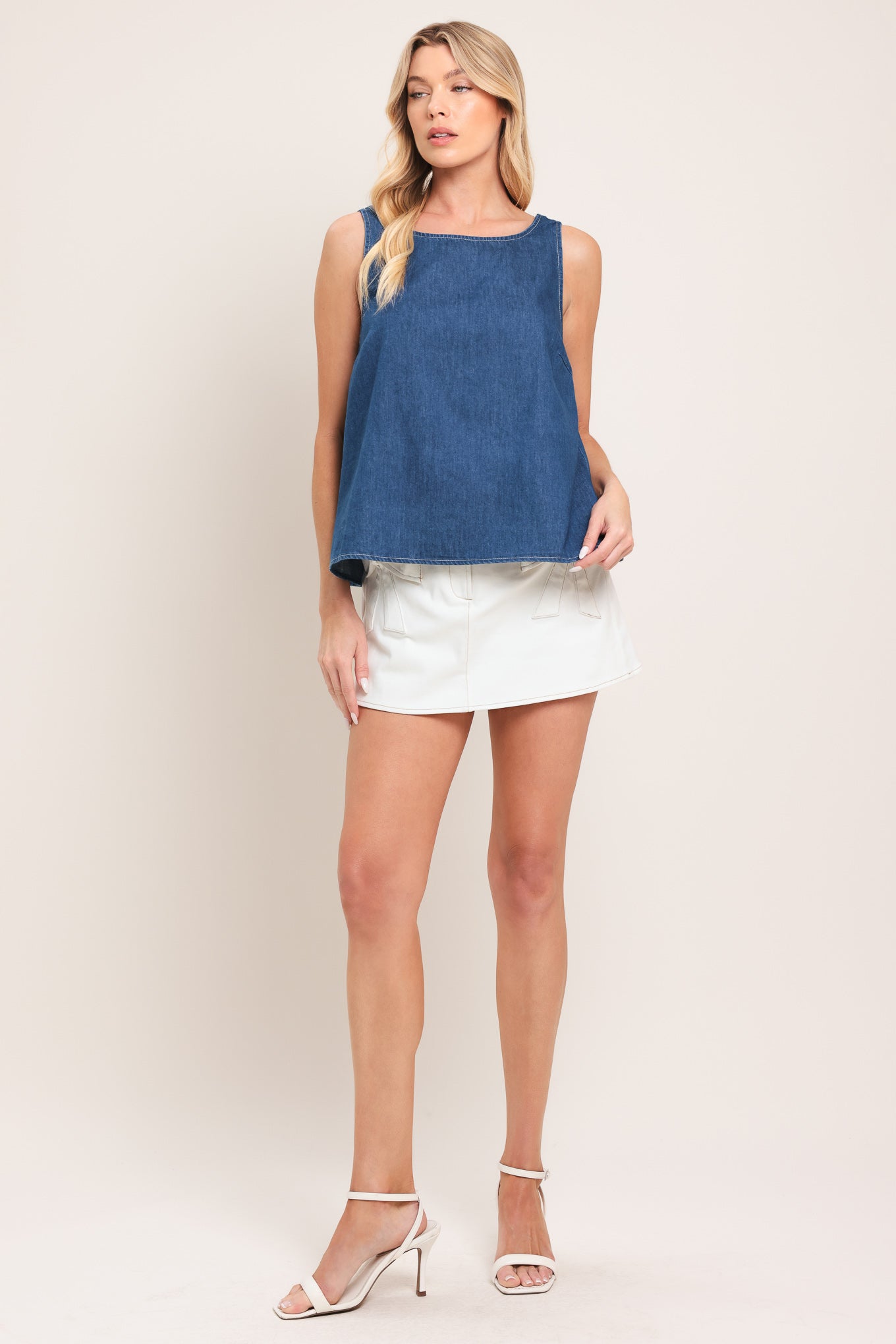 Woman wearing a blue sleeveless denim top featuring round neckline and an open back with a bow | Flying Tomato