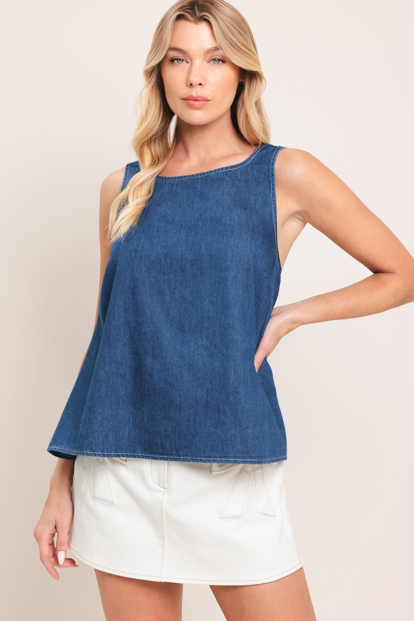Woman wearing a blue sleeveless denim top featuring round neckline and an open back with a bow | Flying Tomato