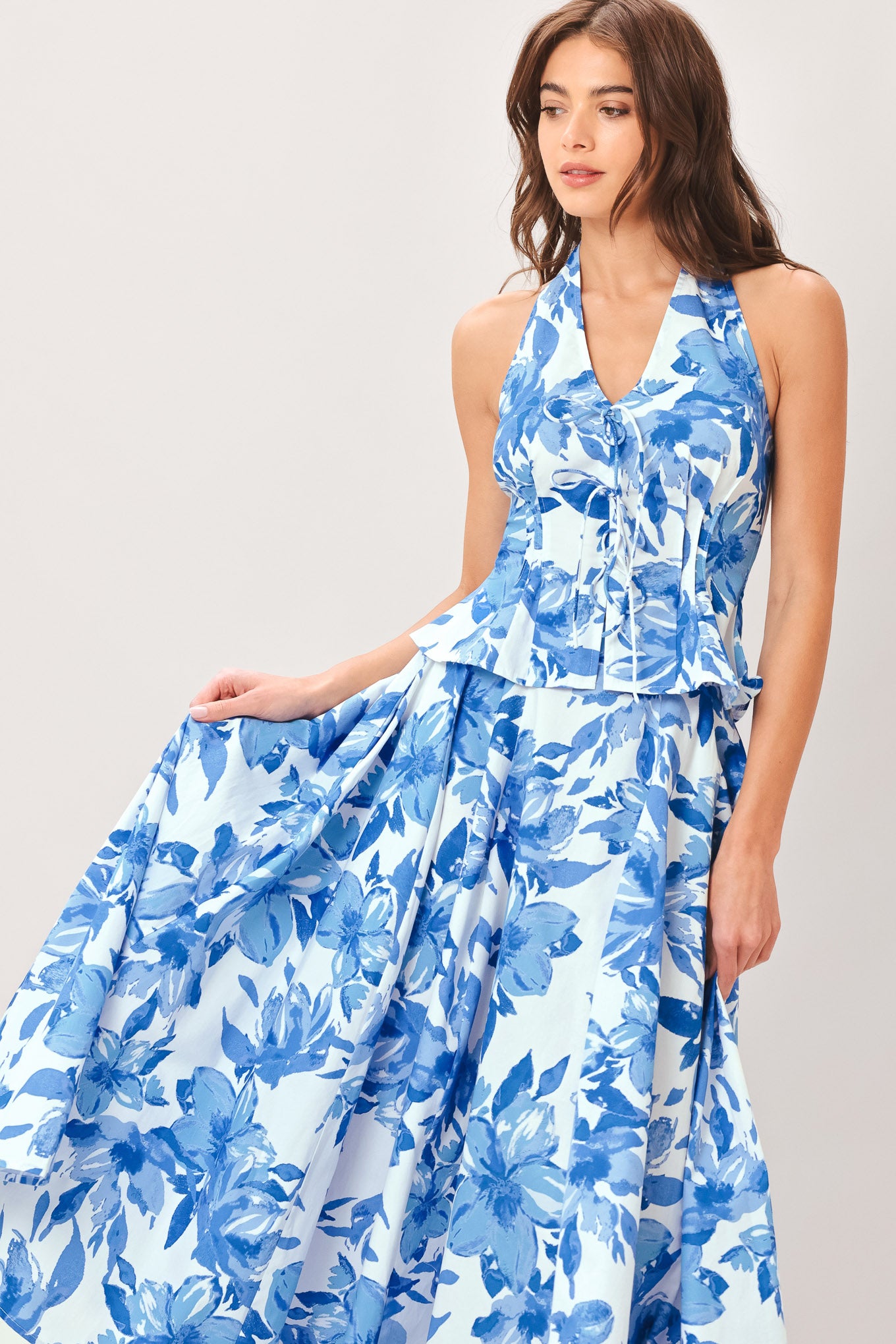 Woman wearing a blue floral top and skirt featuring V halter neckline, corset waist, front tie, peplum and back zipper closure | Flying Tomato