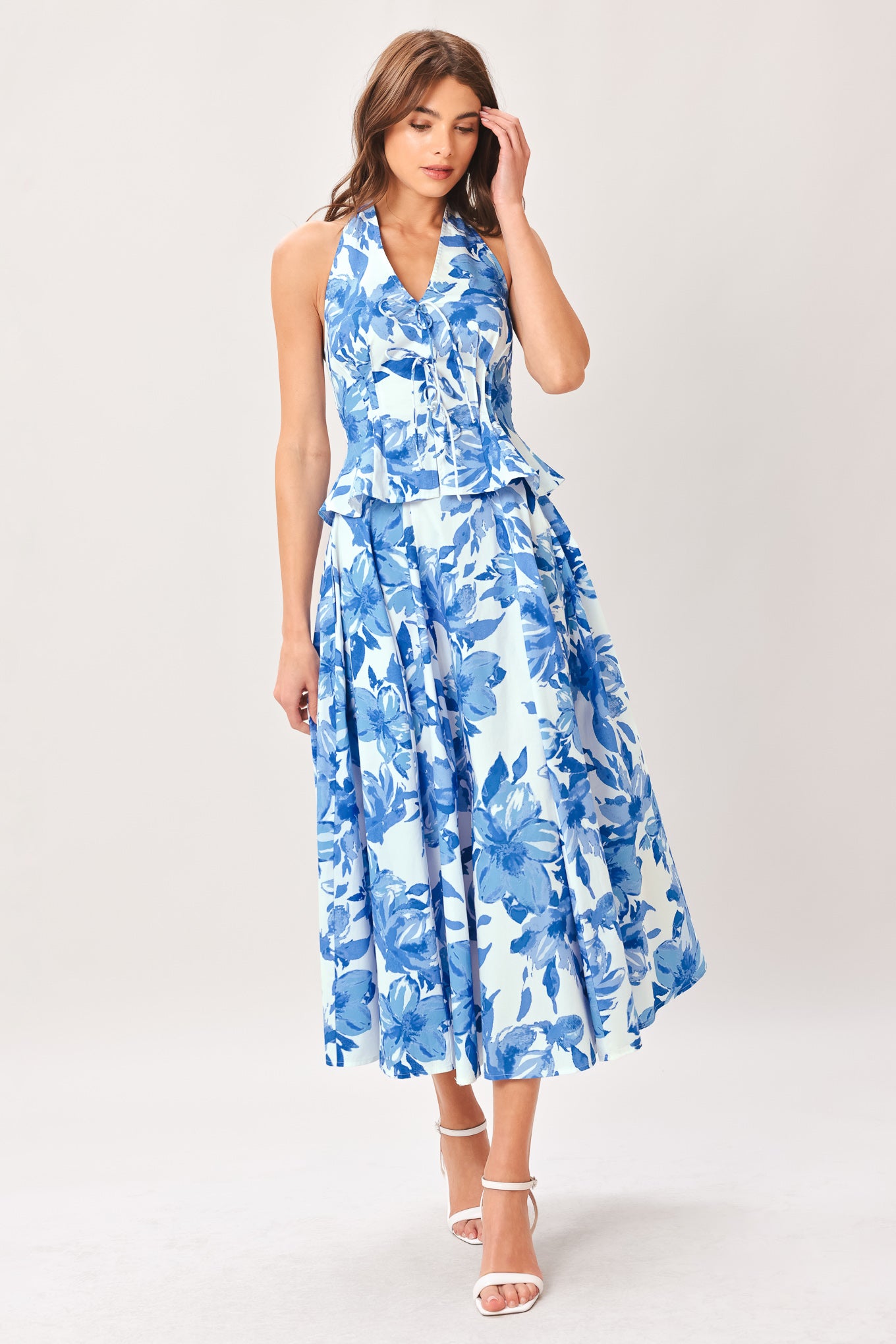 Woman wearing a blue floral top and skirt featuring V halter neckline, corset waist, front tie, peplum and back zipper closure | Flying Tomato