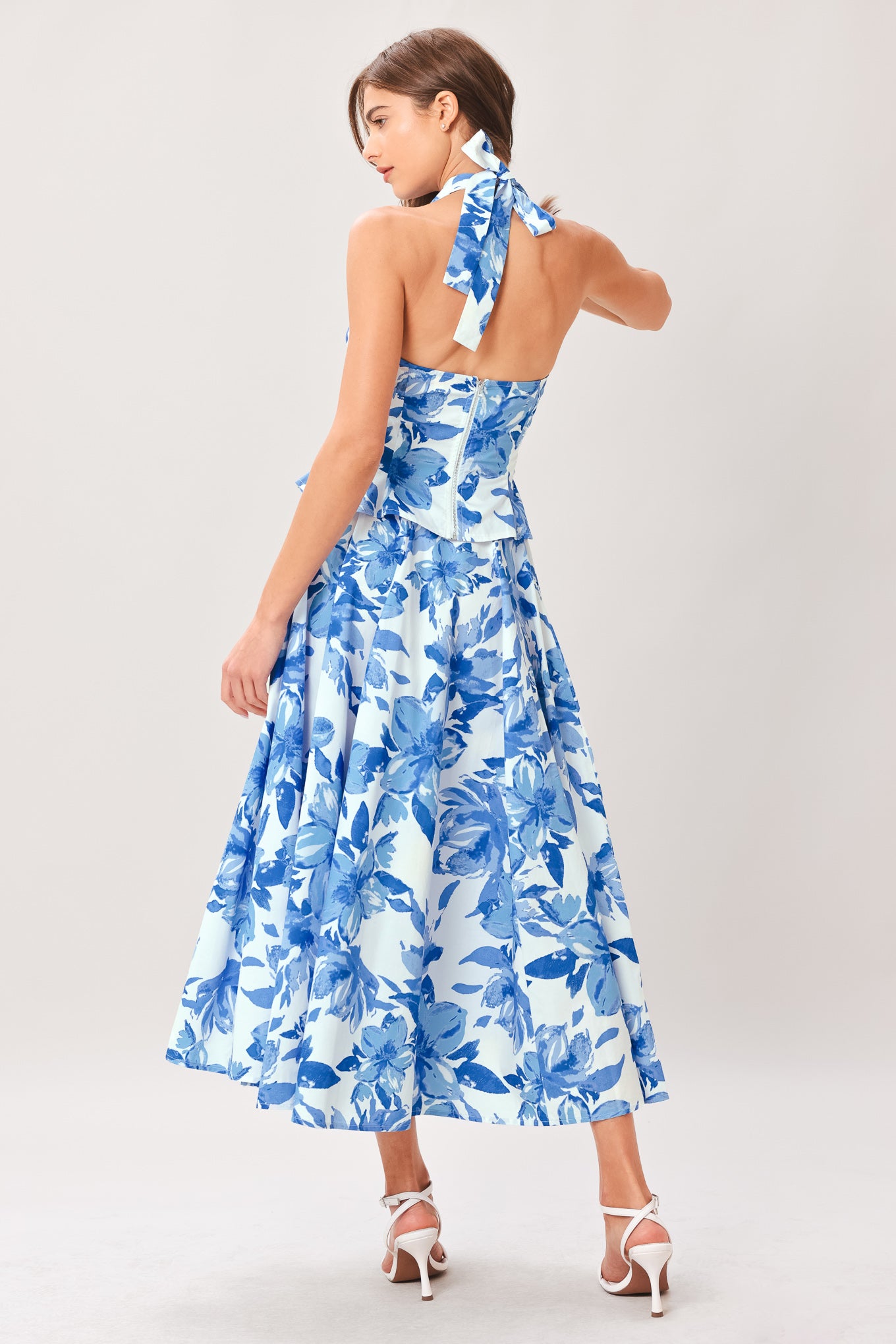 Woman wearing a blue floral top and skirt featuring V halter neckline, corset waist, front tie, peplum and back zipper closure | Flying Tomato