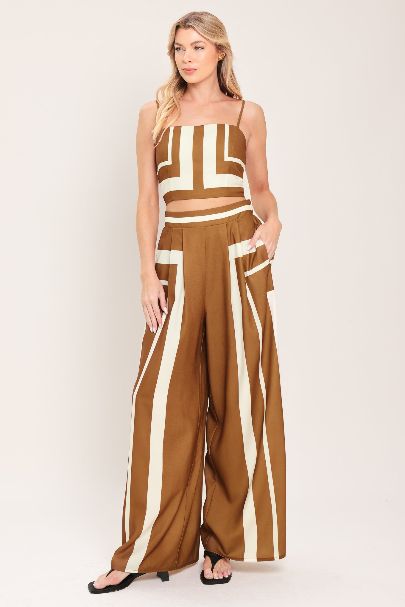 Woman wearing a brown and white geometrical top and pant set featuring crop top with straps and smocked back bodice, wide leg pant with elastic back | Flying Tomato