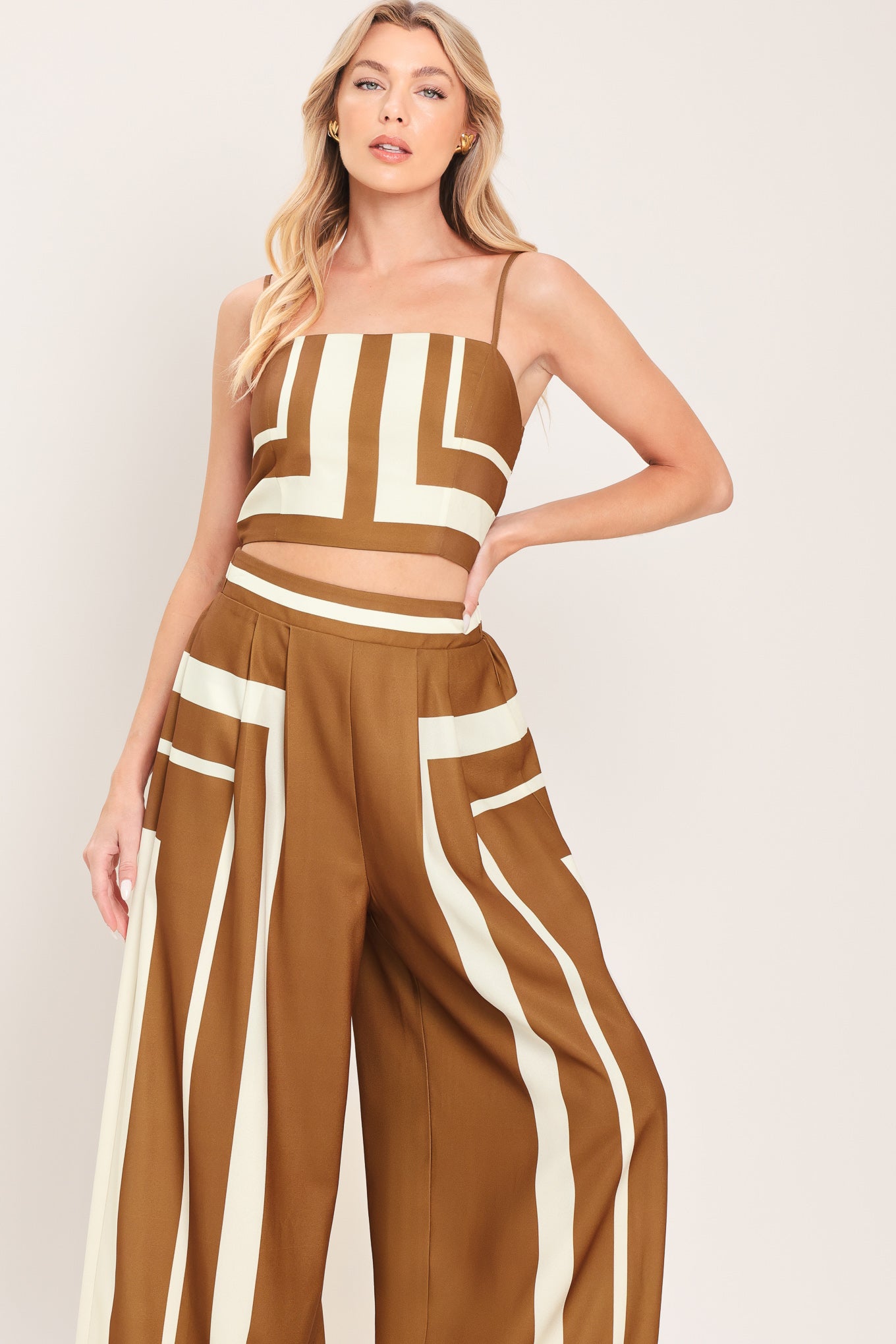 Woman wearing a brown and white geometrical top and pant set featuring crop top with straps and smocked back bodice, wide leg pant with elastic back | Flying Tomato
