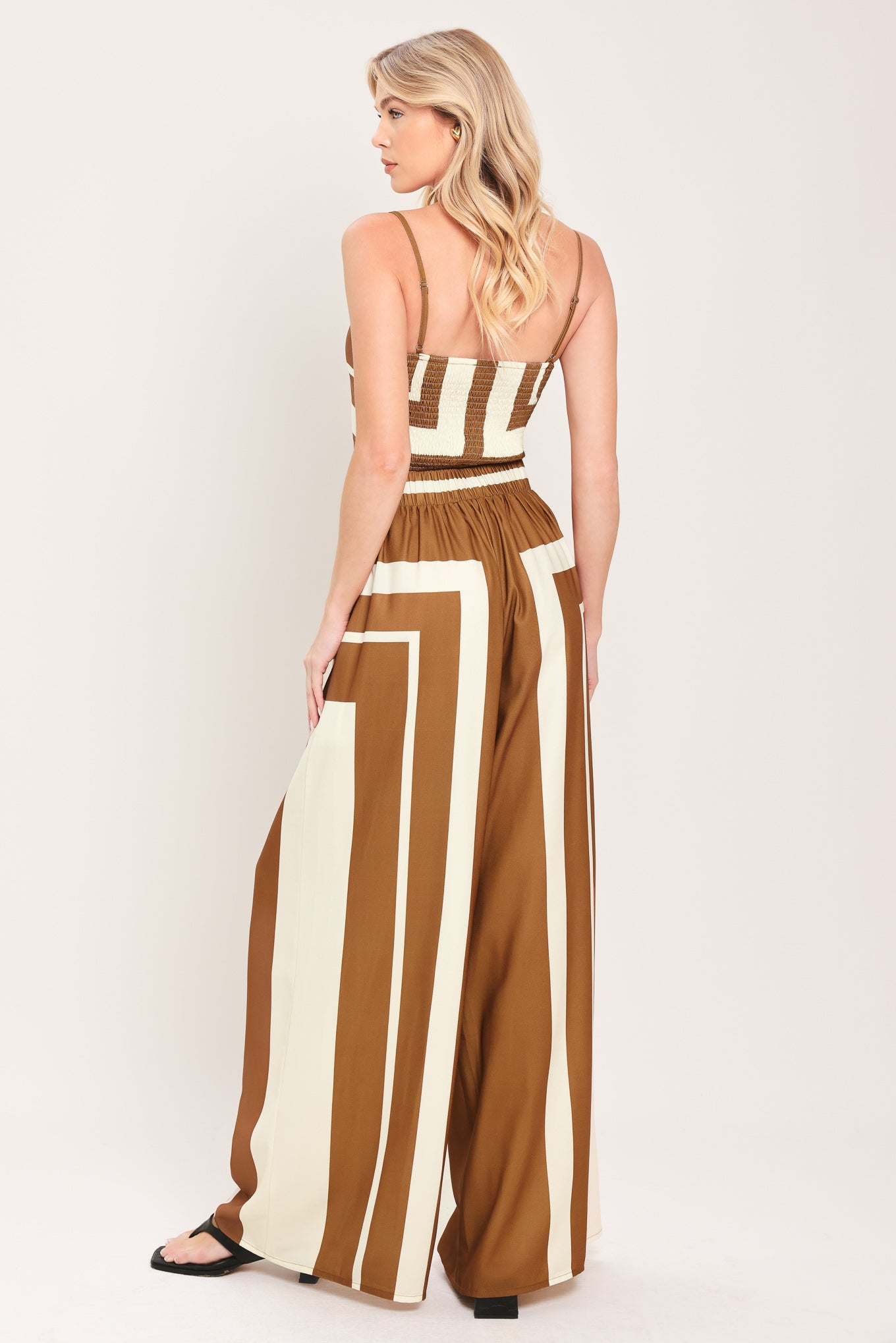 Woman wearing a brown and white geometrical top and pant set featuring crop top with straps and smocked back bodice, wide leg pant with elastic back | Flying Tomato