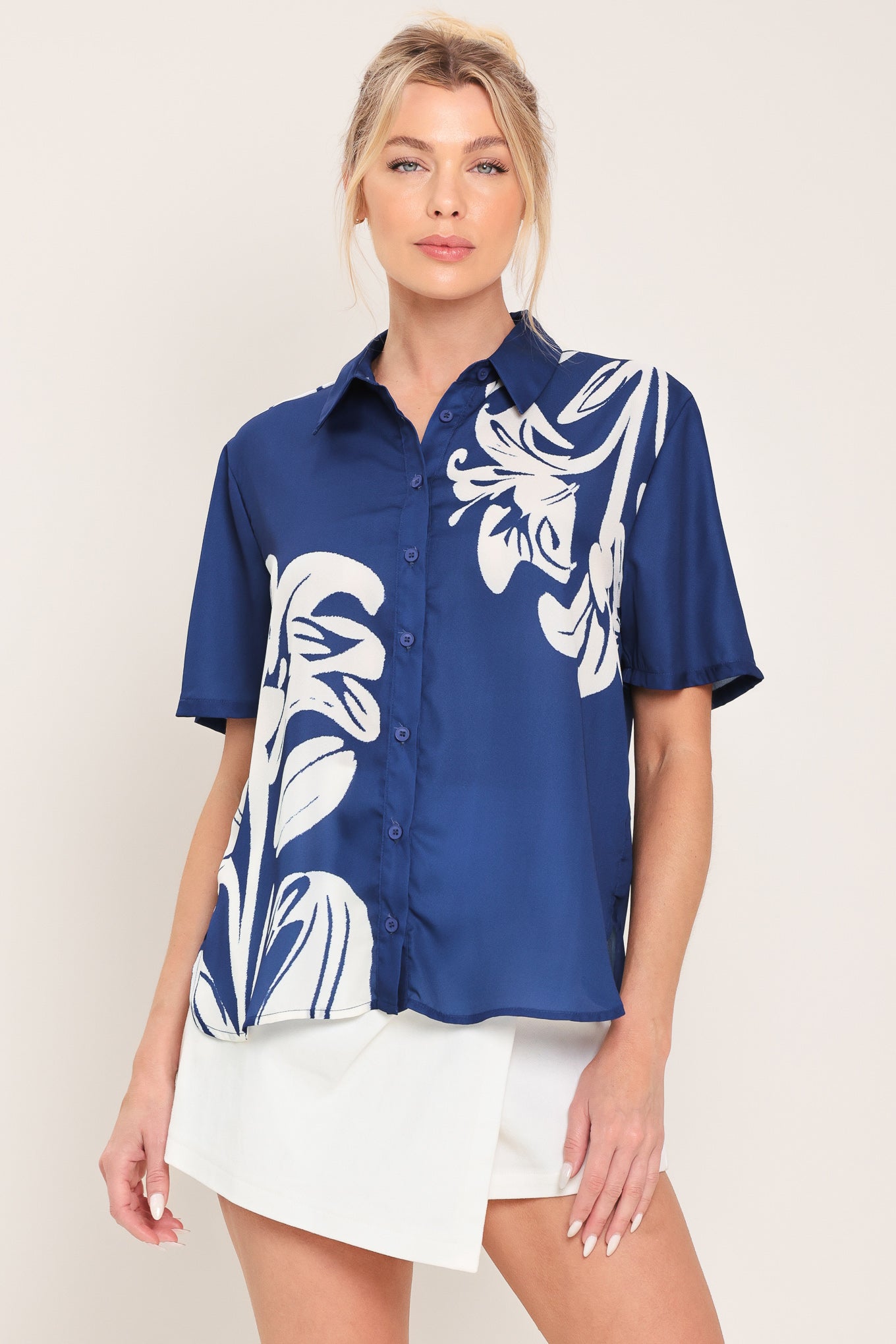 Woman wearing a navy blue with white floral print collared, short-sleeve button down top | Flying Tomato