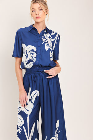 Woman wearing a navy blue with white floral print collared, short-sleeve button down top | Flying Tomato