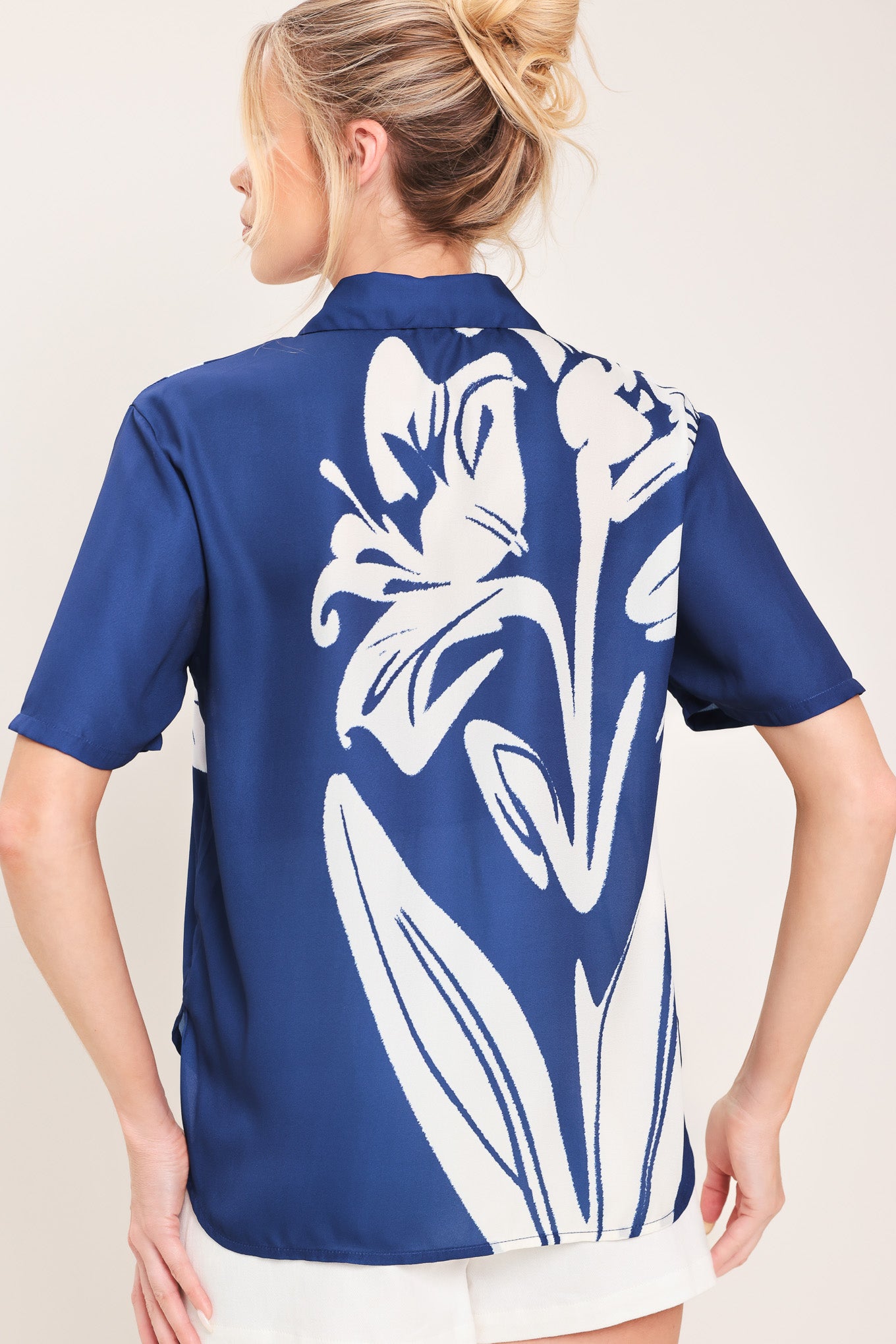 Woman wearing a navy blue with white floral print collared, short-sleeve button down top | Flying Tomato