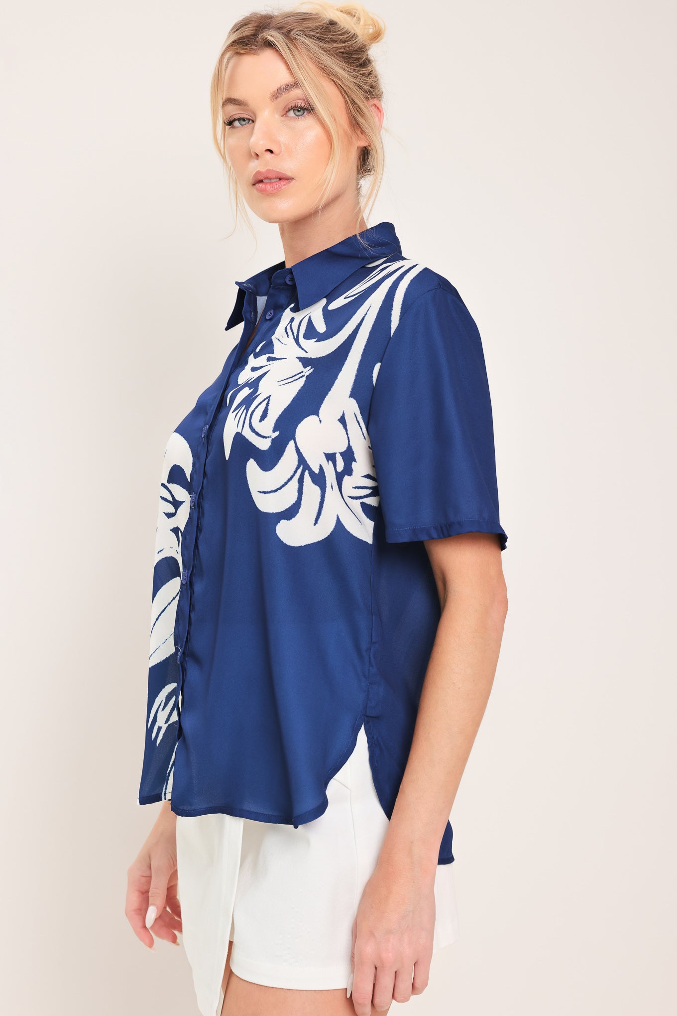 Woman wearing a navy blue with white floral print collared, short-sleeve button down top | Flying Tomato