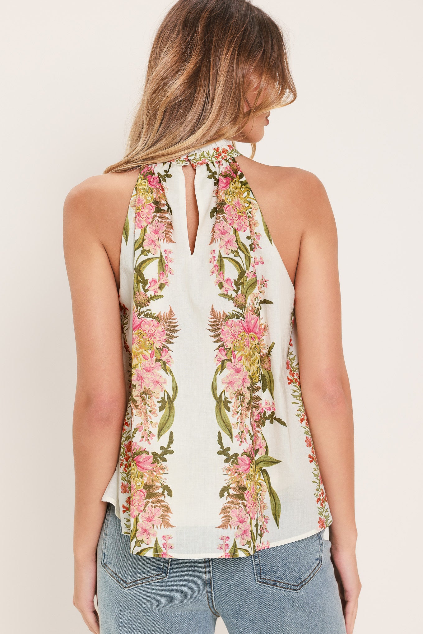 Woman wearing a floral sleeveless woven halter top with back neck button closure | Flying Tomato