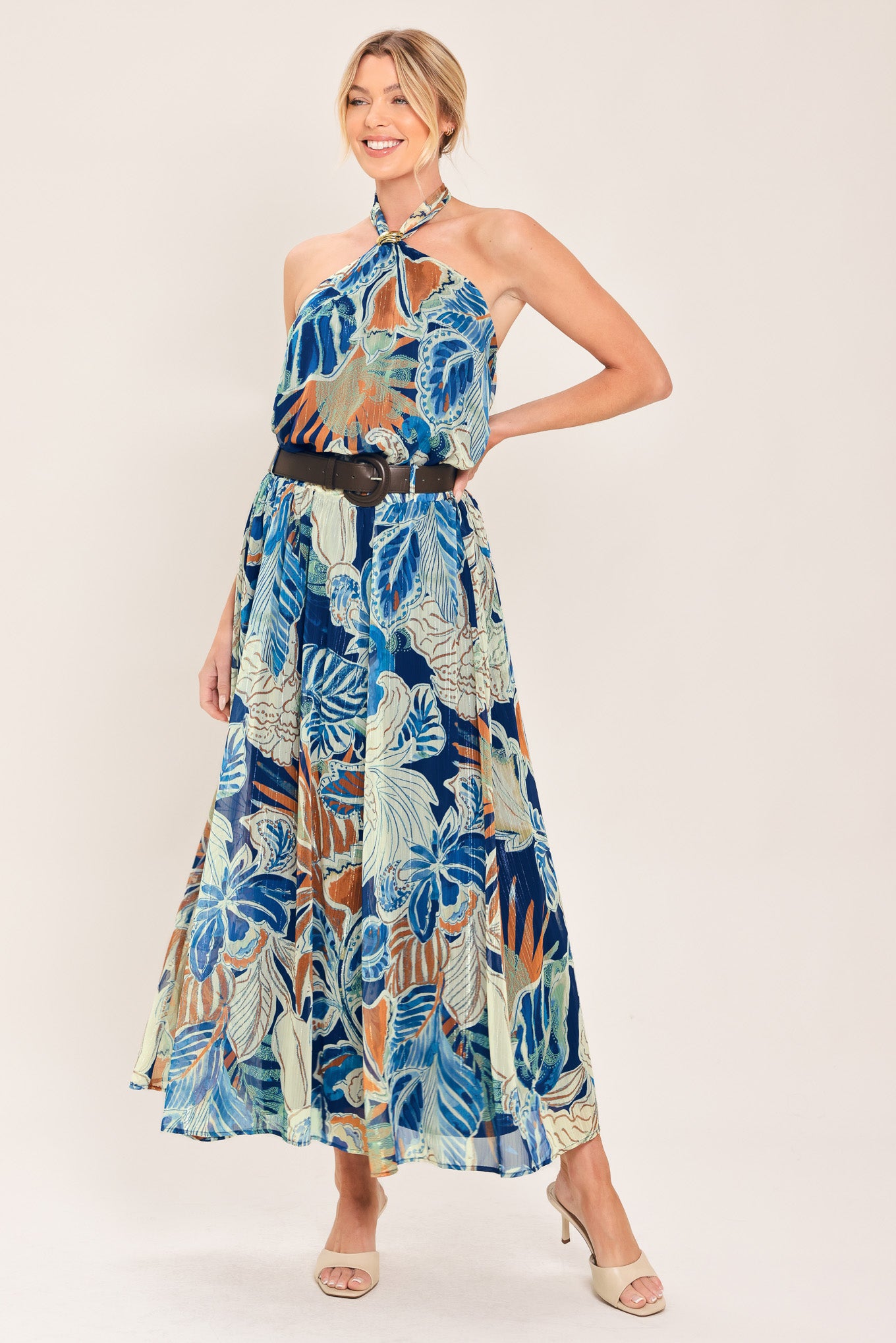 A woman modeling a halter-neck top and maxi skirt with a tropical leaf print in shades of blue, beige, and white, styled with a black belt | Flying Tomato
