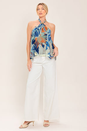 A woman wearing a halter-neck top with a tropical print in shades of blue, orange, and beige | Flying Tomato