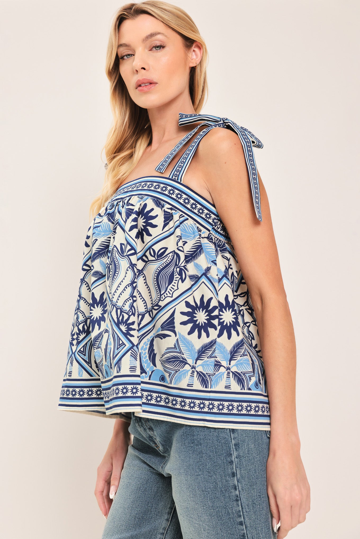 Woman wearing a blue and white patterned top with shoulder ties and smocked back band | Flying Tomato