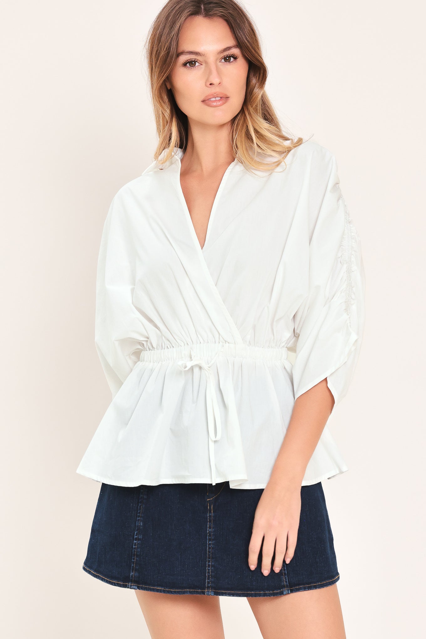 Woman wearing a white top featuring collar, surplice neckline, elastic waist with tie, elbow sleeve with shirring and peplum | Flying Tomato