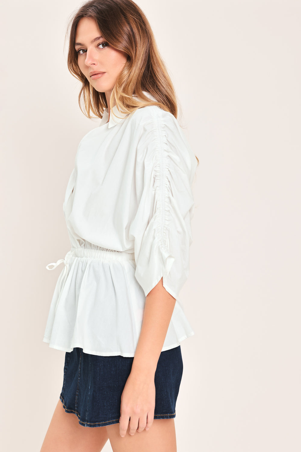 Woman wearing a white top featuring collar, surplice neckline, elastic waist with tie, elbow sleeve with shirring and peplum | Flying Tomato