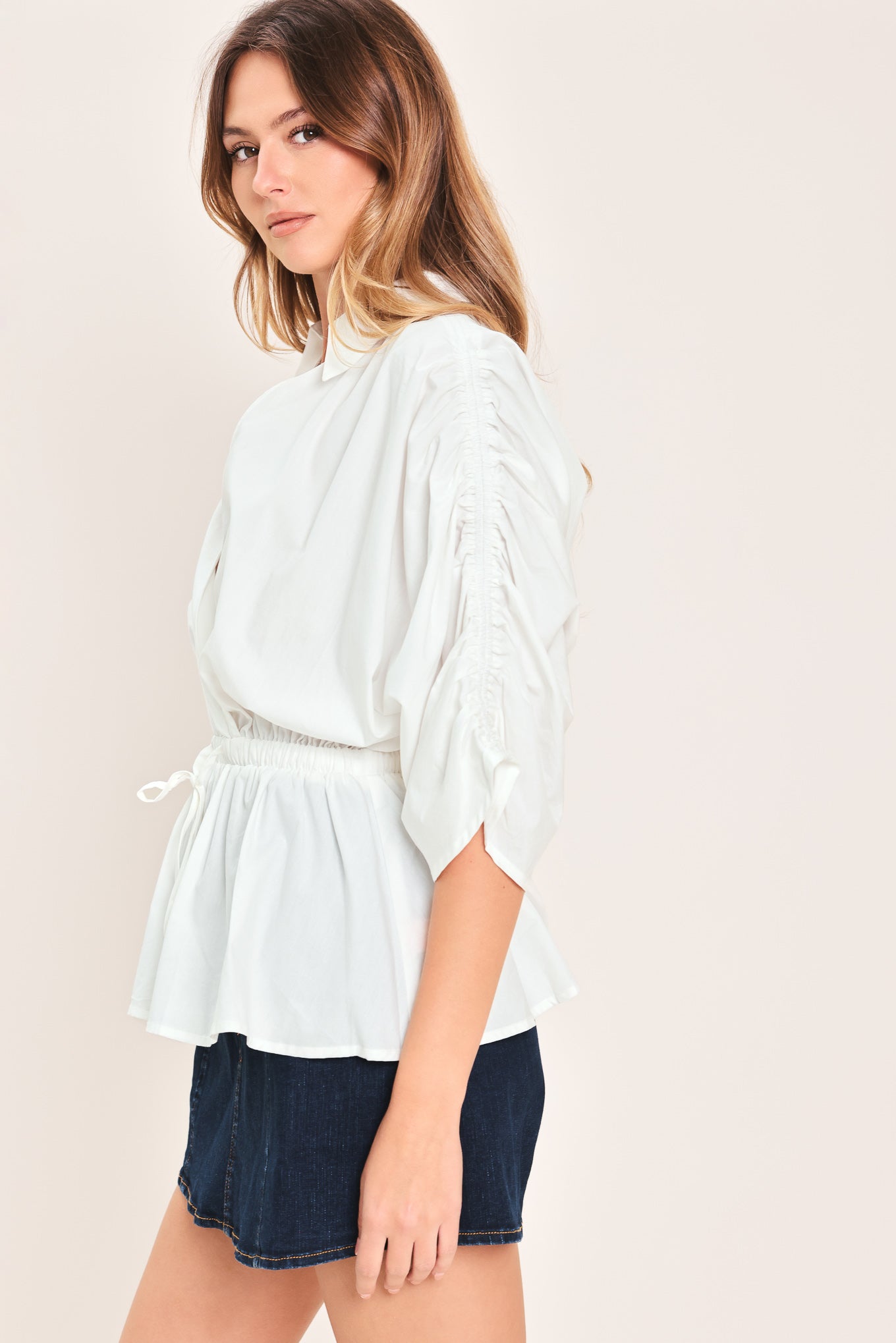 Woman wearing a white top featuring collar, surplice neckline, elastic waist with tie, elbow sleeve with shirring and peplum | Flying Tomato