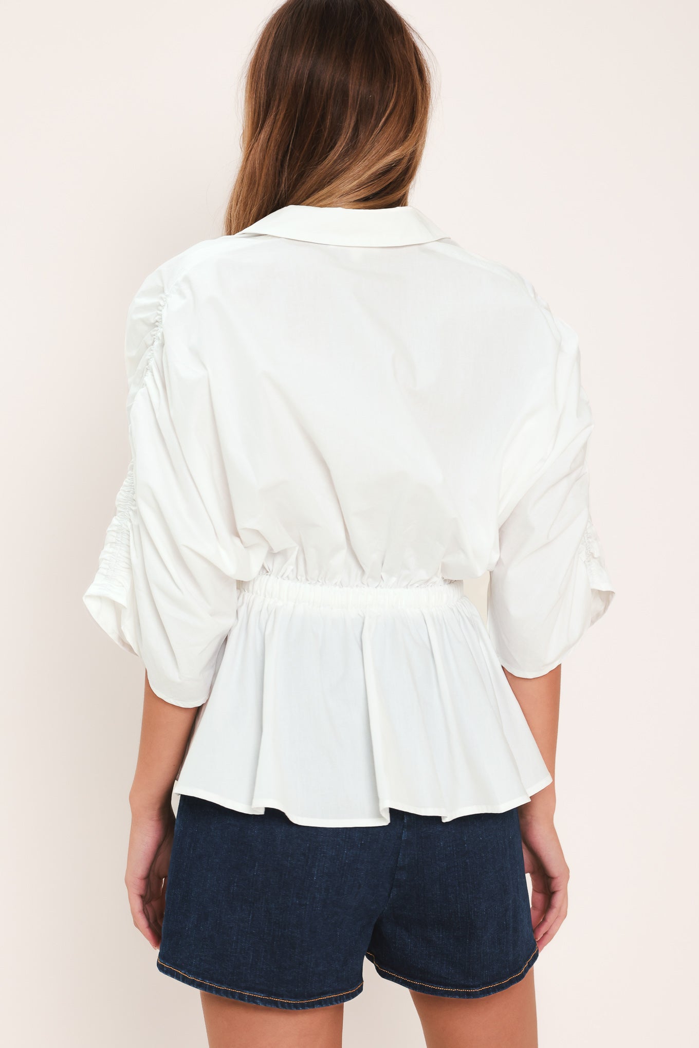 Woman wearing a white top featuring collar, surplice neckline, elastic waist with tie, elbow sleeve with shirring and peplum | Flying Tomato