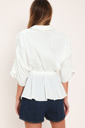 Woman wearing a white top featuring collar, surplice neckline, elastic waist with tie, elbow sleeve with shirring and peplum | Flying Tomato