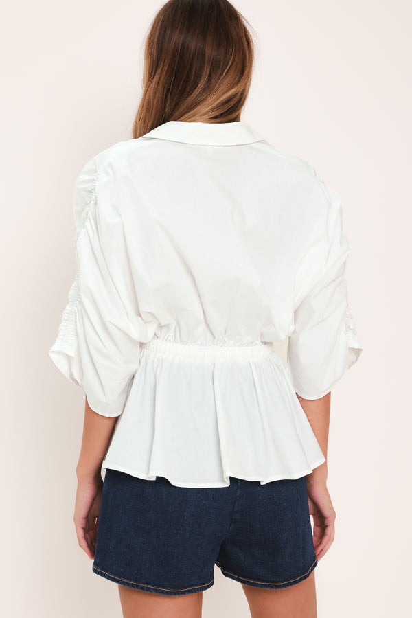 Woman wearing a white top featuring collar, surplice neckline, elastic waist with tie, elbow sleeve with shirring and peplum | Flying Tomato