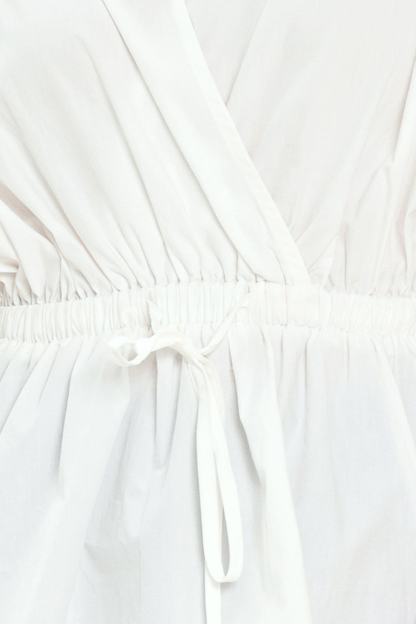 Woman wearing a white top featuring collar, surplice neckline, elastic waist with tie, elbow sleeve with shirring and peplum | Flying Tomato
