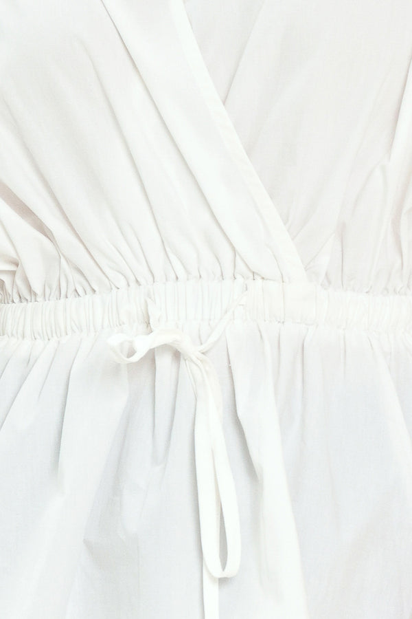 Woman wearing a white top featuring collar, surplice neckline, elastic waist with tie, elbow sleeve with shirring and peplum | Flying Tomato