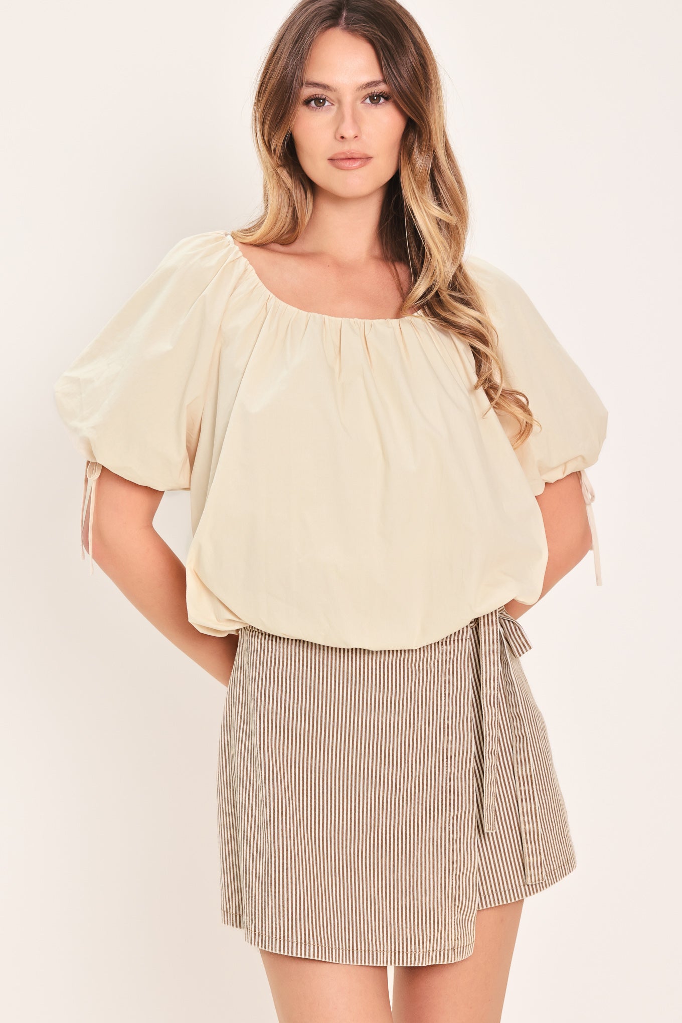 Woman wearing a light-beige stone top featuring wide neckline, short puff sleeve with tie and balloon waist | Flying Tomato