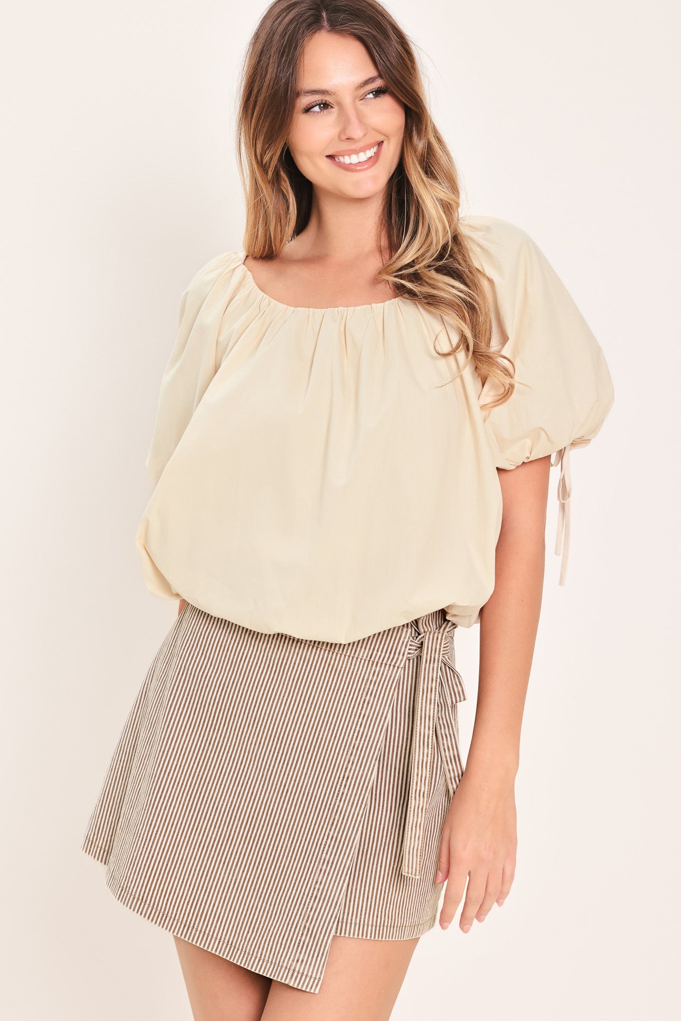 Woman wearing a light-beige stone top featuring wide neckline, short puff sleeve with tie and balloon waist | Flying Tomato