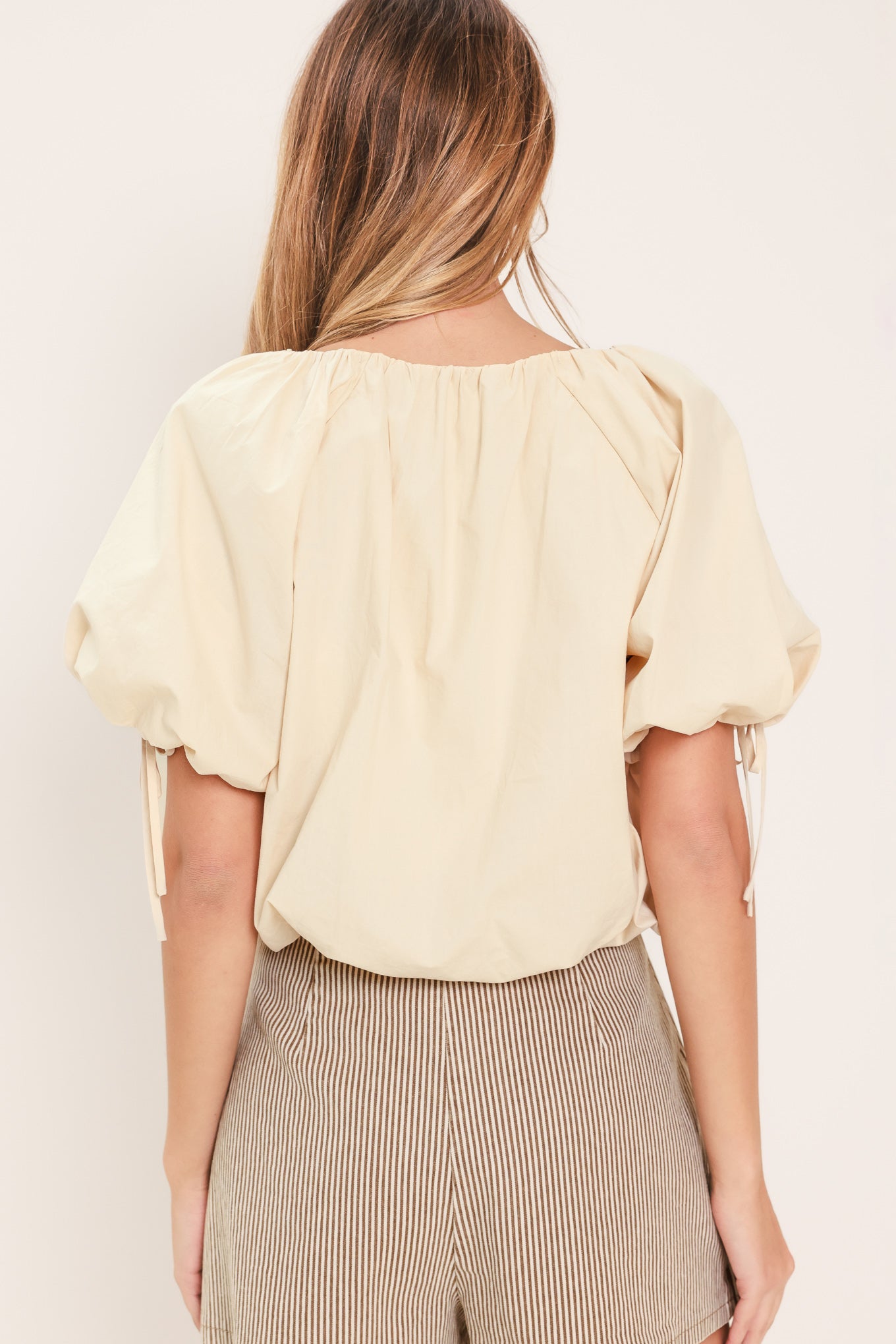 Woman wearing a light-beige stone top featuring wide neckline, short puff sleeve with tie and balloon waist | Flying Tomato