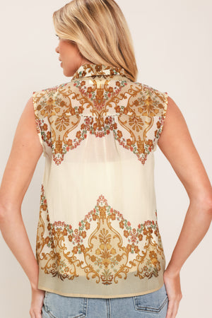 A woman wearing a sleeveless cream-colored blouse with a brown and gold damask pattern and a large bow tie-neck | Flying Tomato