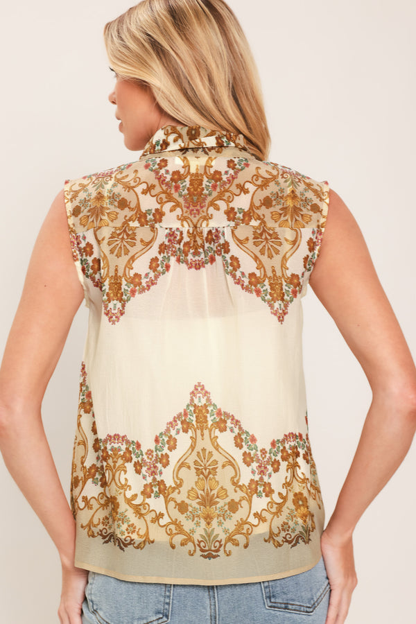 A woman wearing a sleeveless cream-colored blouse with a brown and gold damask pattern and a large bow tie-neck | Flying Tomato