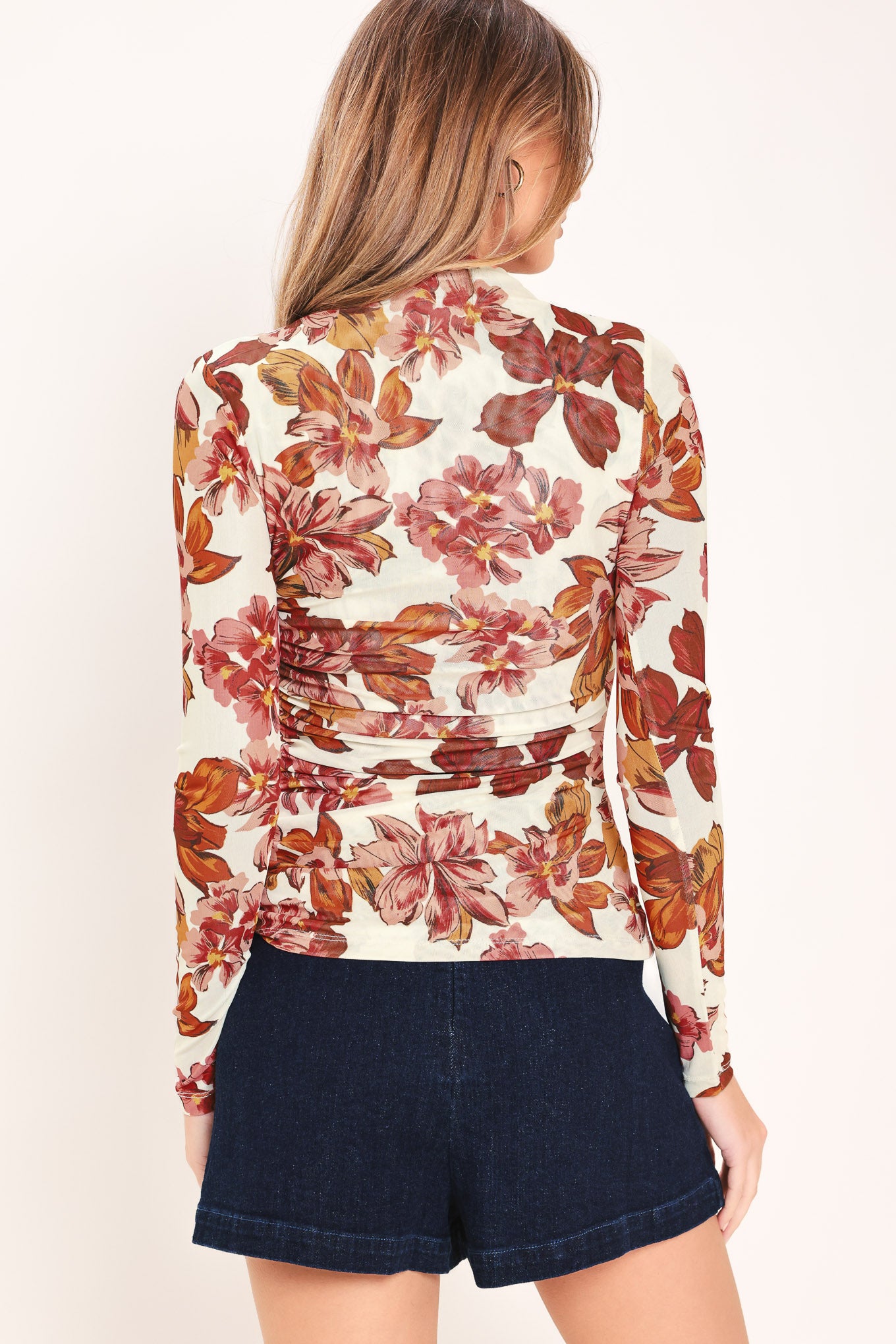 Woman wearing a long sleeve ivory and mauve floral printed woven mesh top with funnel neckline, side shirring | Flying Tomato