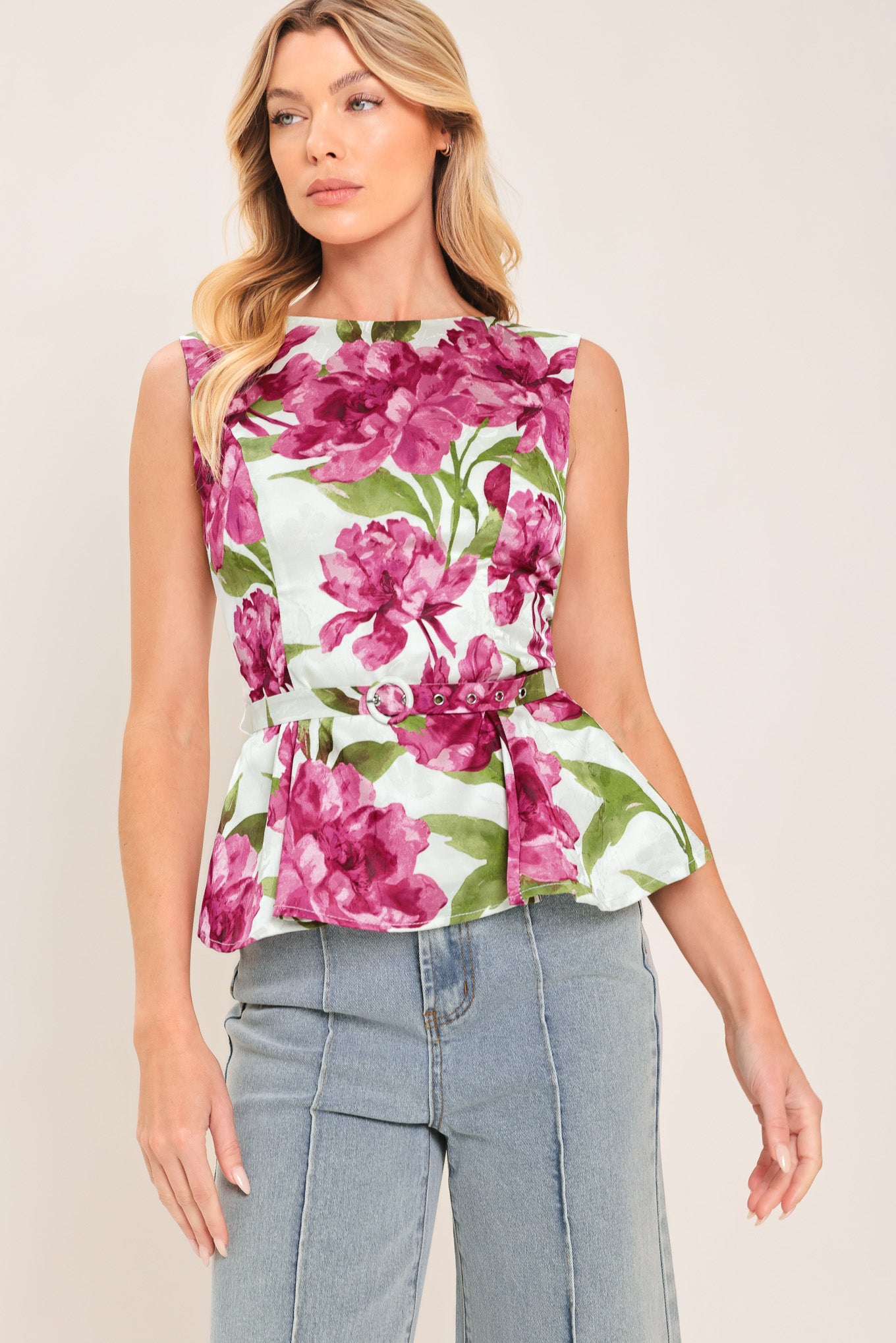 A woman wearing a sleeveless white peplum top with a vibrant pink and green floral print | Flying Tomato