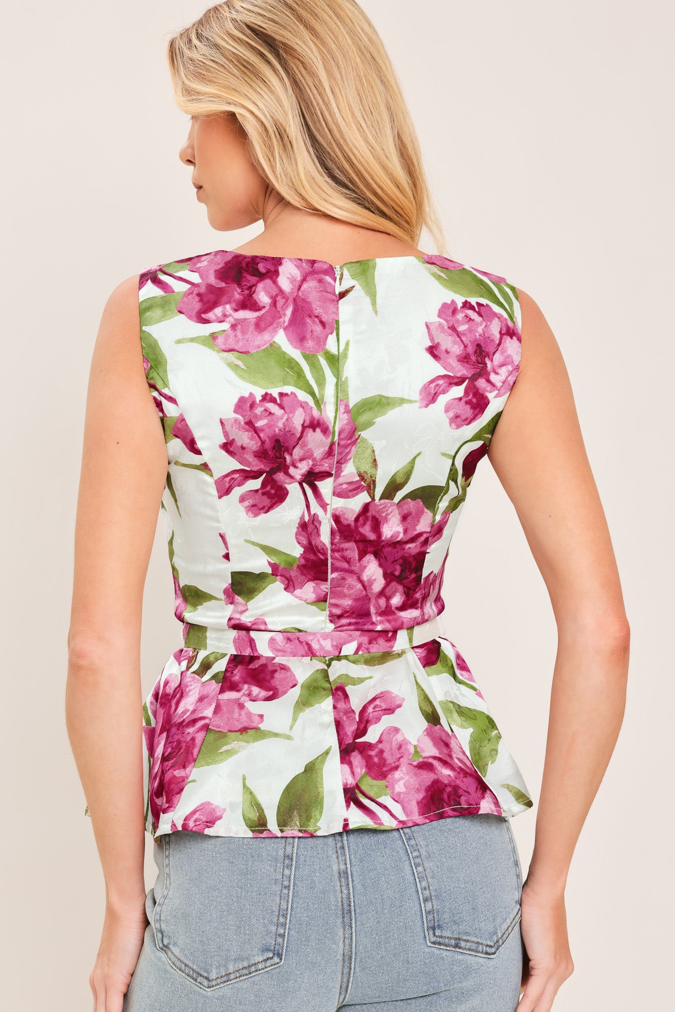 A woman wearing a sleeveless white peplum top with a vibrant pink and green floral print | Flying Tomato