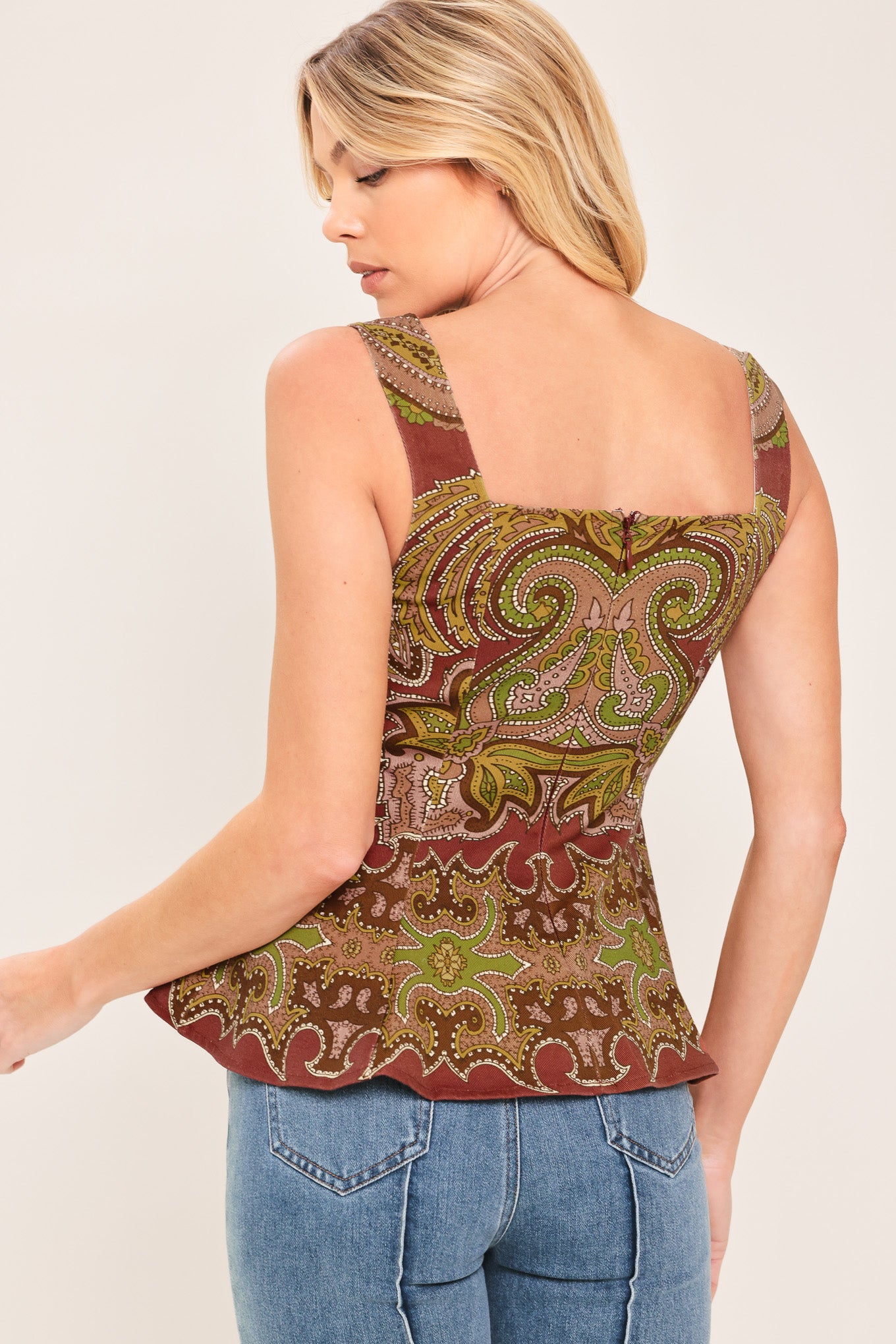 A woman wearing a sleeveless peplum top with a brown, olive green, and beige paisley pattern | Flying Tomato