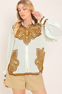 Woman wearing a white long sleeve  button down blouse with brown leaf-like print | Flying Tomato