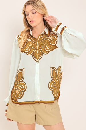 Woman wearing a white long sleeve  button down blouse with brown leaf-like print | Flying Tomato