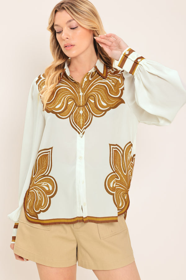 Woman wearing a white long sleeve  button down blouse with brown leaf-like print | Flying Tomato