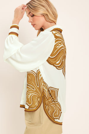 Woman wearing a white long sleeve  button down blouse with brown leaf-like print | Flying Tomato