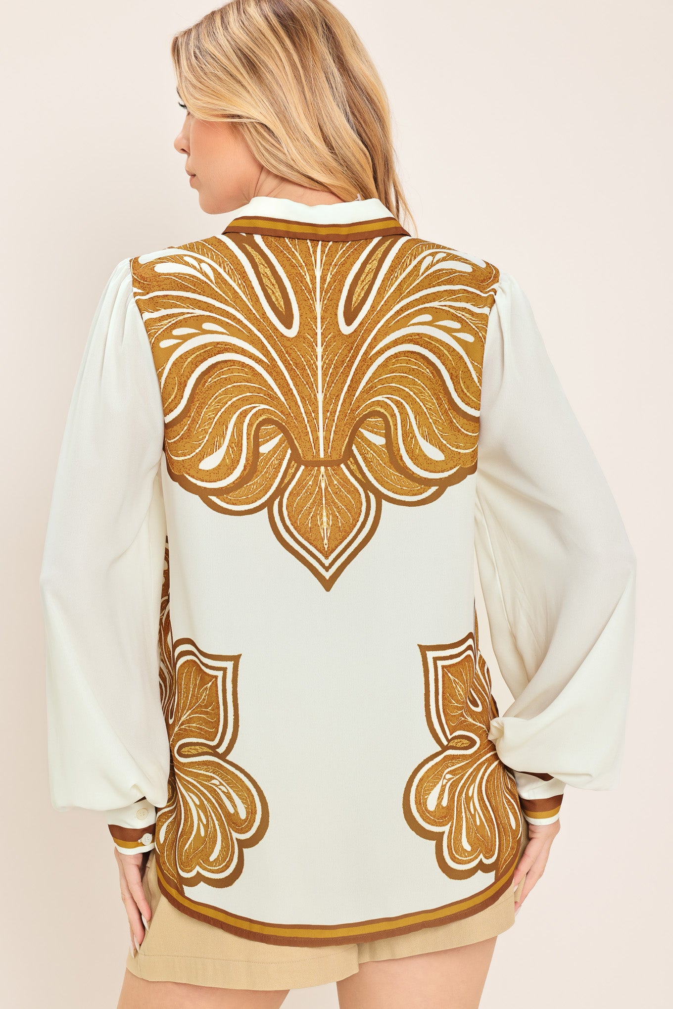 Woman wearing a white long sleeve  button down blouse with brown leaf-like print | Flying Tomato