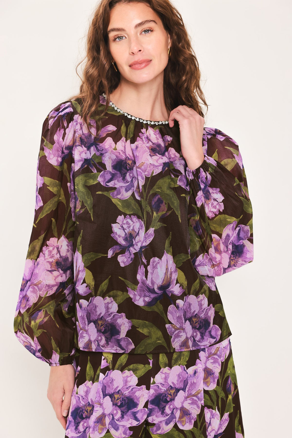 A woman wearing a dark brown sheer long-sleeve top with a vibrant purple and green floral print | Flying Tomato