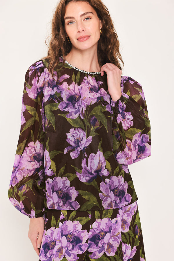 A woman wearing a dark brown sheer long-sleeve top with a vibrant purple and green floral print | Flying Tomato