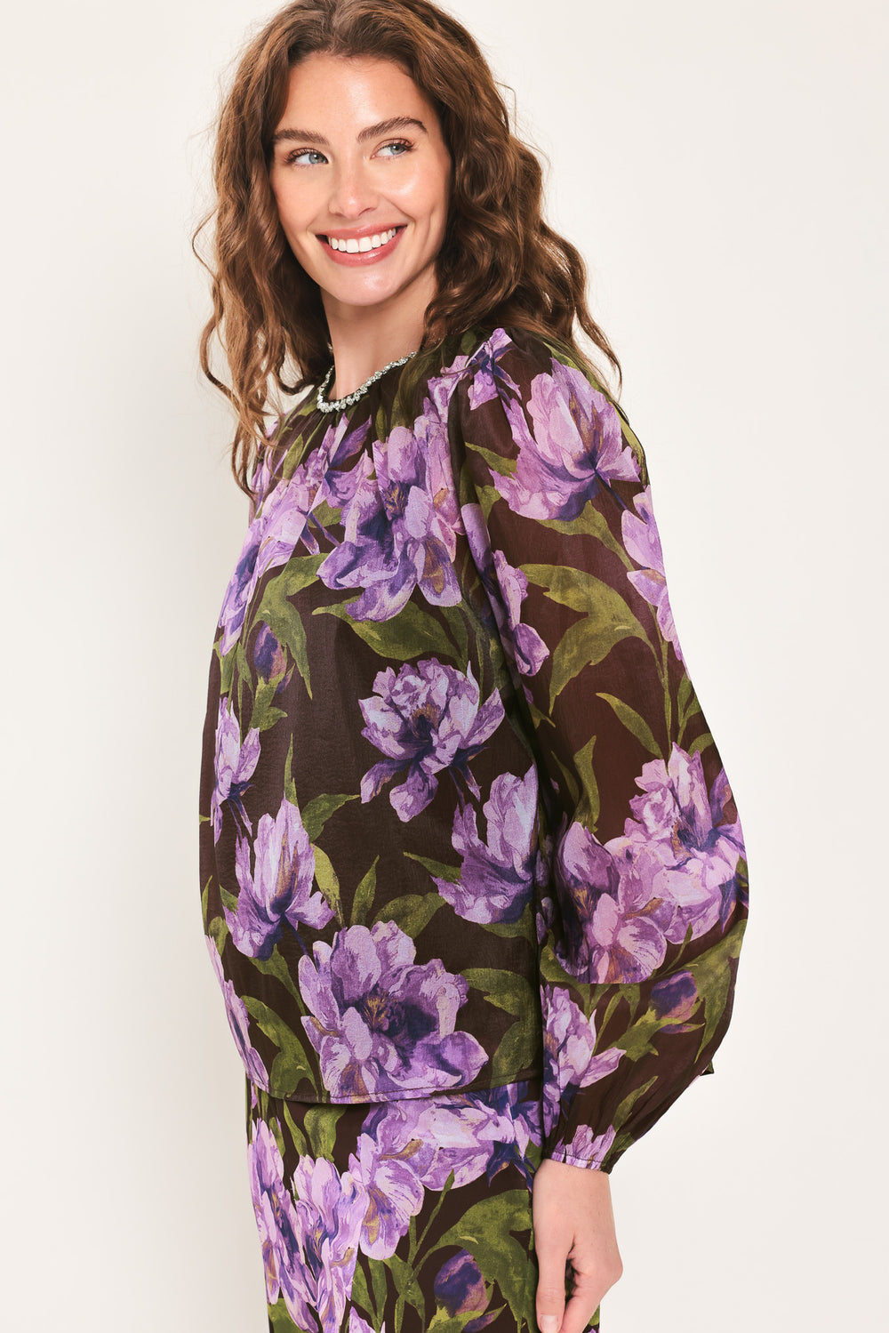 A woman wearing a dark brown sheer long-sleeve top with a vibrant purple and green floral print | Flying Tomato