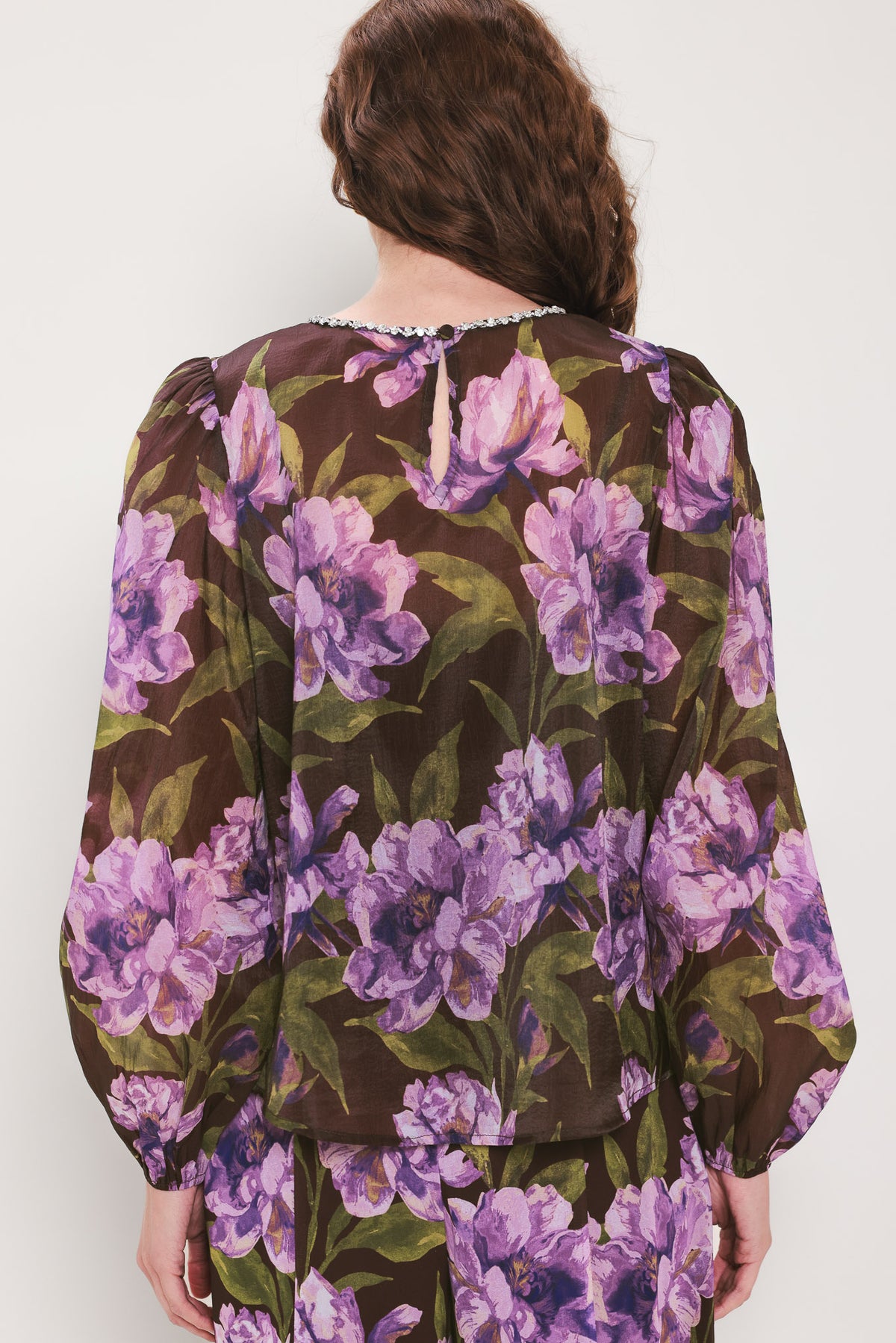 A woman wearing a dark brown sheer long-sleeve top with a vibrant purple and green floral print | Flying Tomato