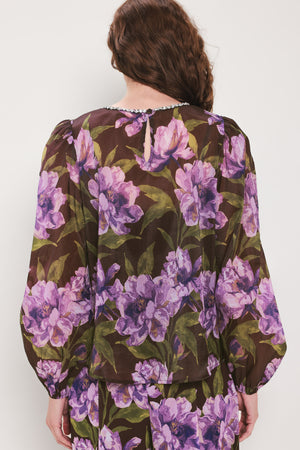 A woman wearing a dark brown sheer long-sleeve top with a vibrant purple and green floral print | Flying Tomato