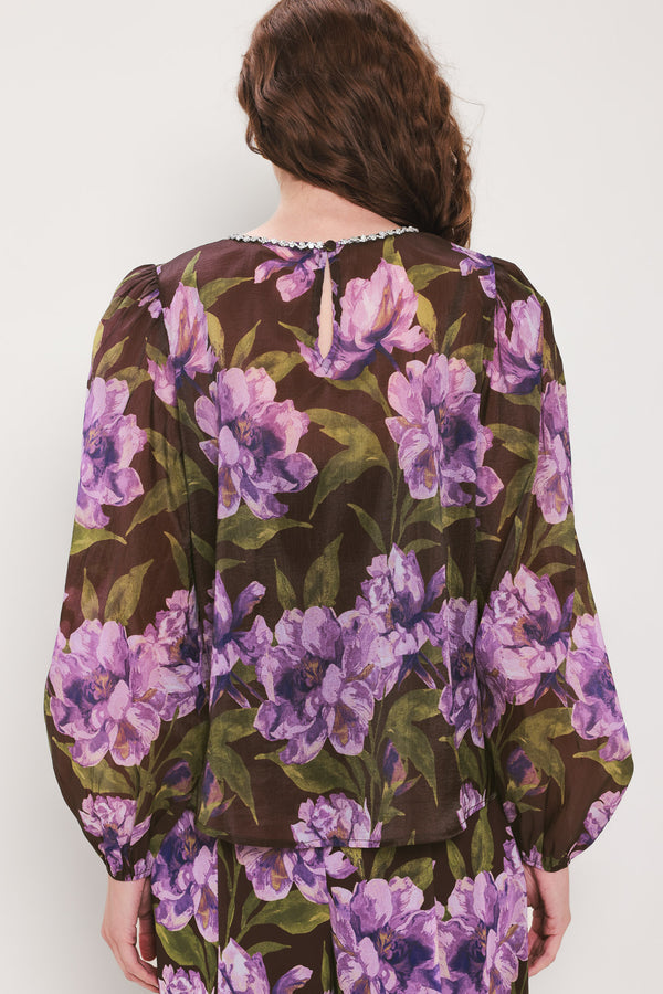 A woman wearing a dark brown sheer long-sleeve top with a vibrant purple and green floral print | Flying Tomato