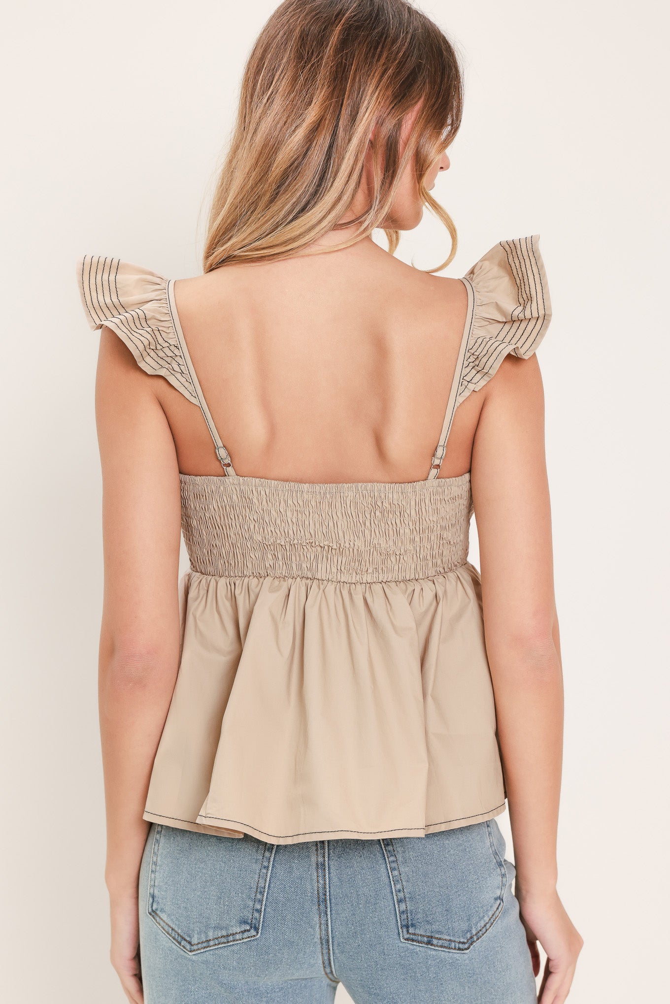 Woman wearing a beige top with ruffled sleeves featuring sweetheart neckline, peplum and smocked back bodice | Flying Tomato