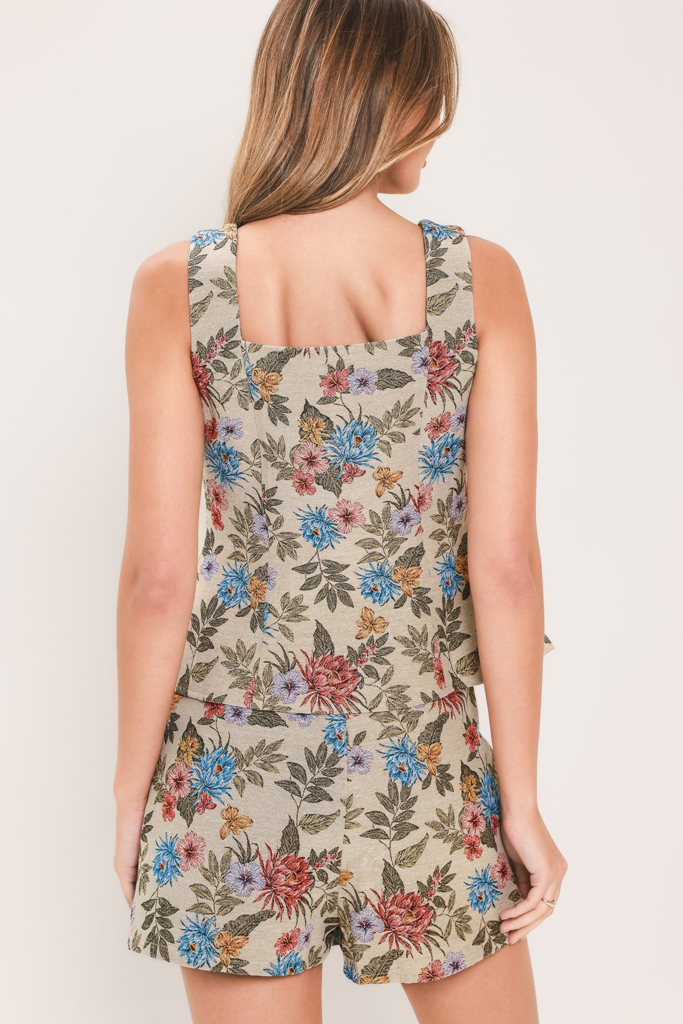 Woman wearing a beige sleeveless woven jacquard top with sweetheart neckline, front button closure and peplum waist. It has pink and blue flowers embroidered on | Flying Tomato
