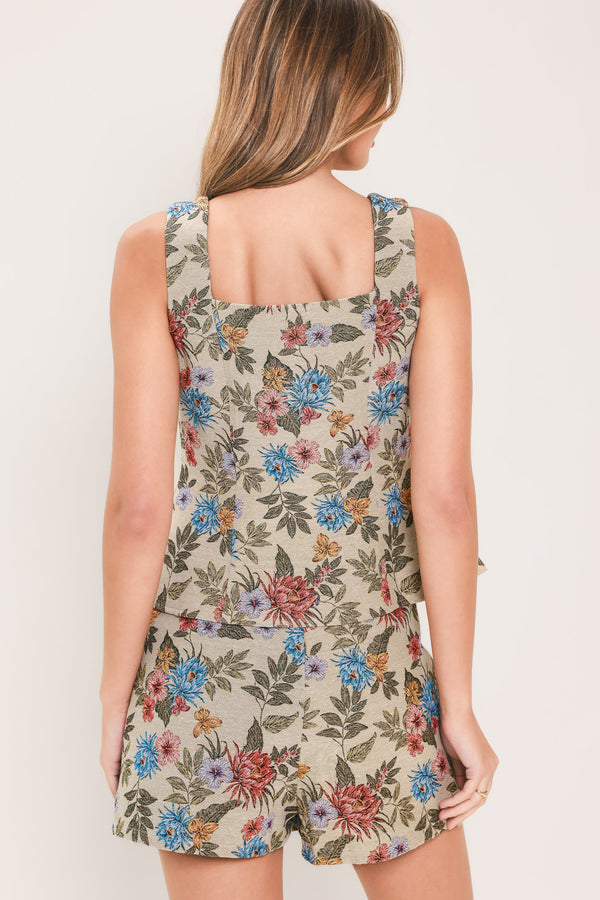 Woman wearing a beige sleeveless woven jacquard top with sweetheart neckline, front button closure and peplum waist. It has pink and blue flowers embroidered on | Flying Tomato