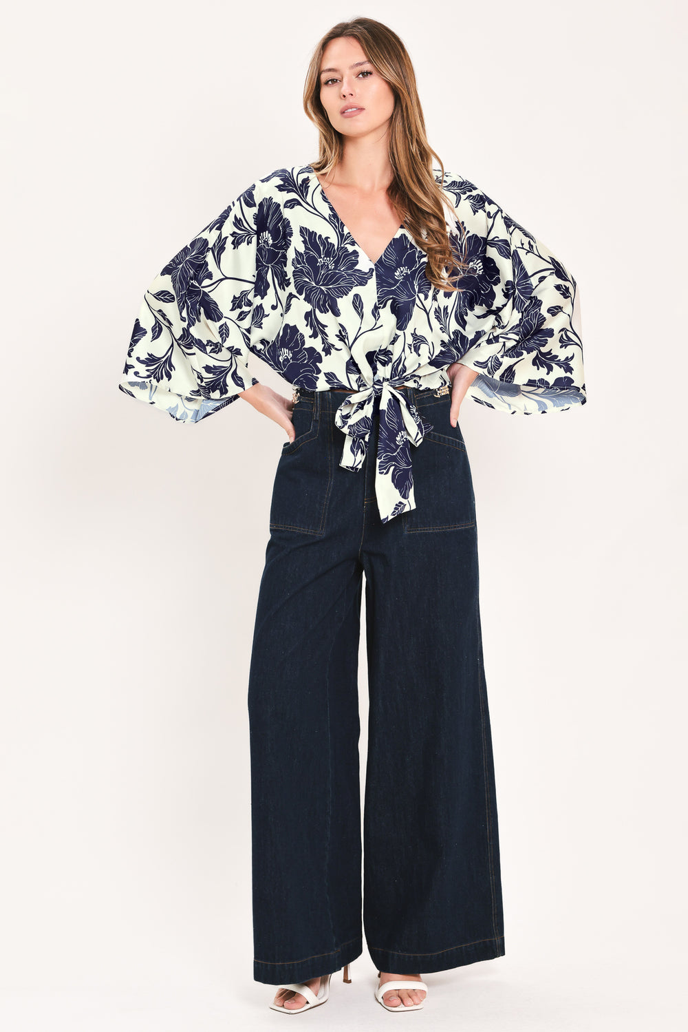 A woman wearing a navy blue and off-white floral print wrap top with wide bell sleeves and a tie waist | Flying Tomato