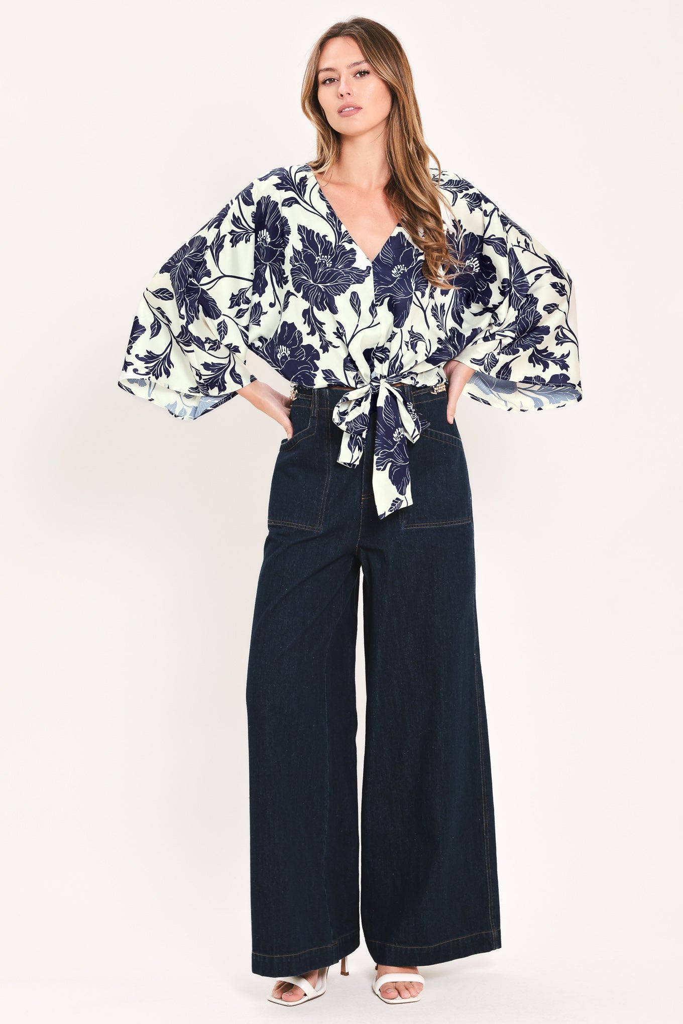 A woman wearing a navy blue and off-white floral print wrap top with wide bell sleeves and a tie waist | Flying Tomato