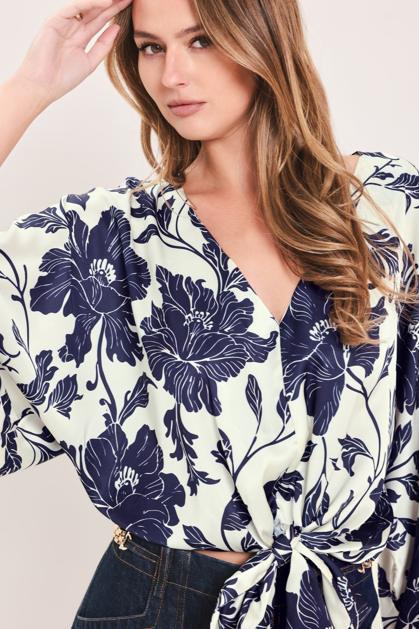 A woman wearing a navy blue and off-white floral print wrap top with wide bell sleeves and a tie waist | Flying Tomato
